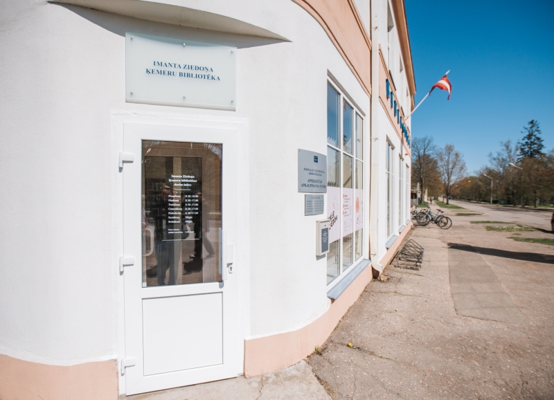 Imanta Ziedoņa Ķemeru bibliotēkas ieeja ar plāksni un darba laiku.