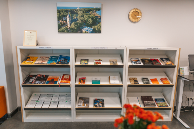 Bibliotēkas grāmatu plaukti, kuros ar vākiem uz priekšu izstādītas grāmatas