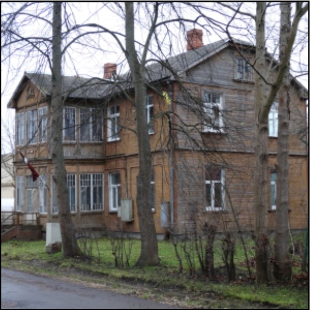 Vēsturiska divstāvu koka ēka ar verandām un Latvijas karogu pie fasādes